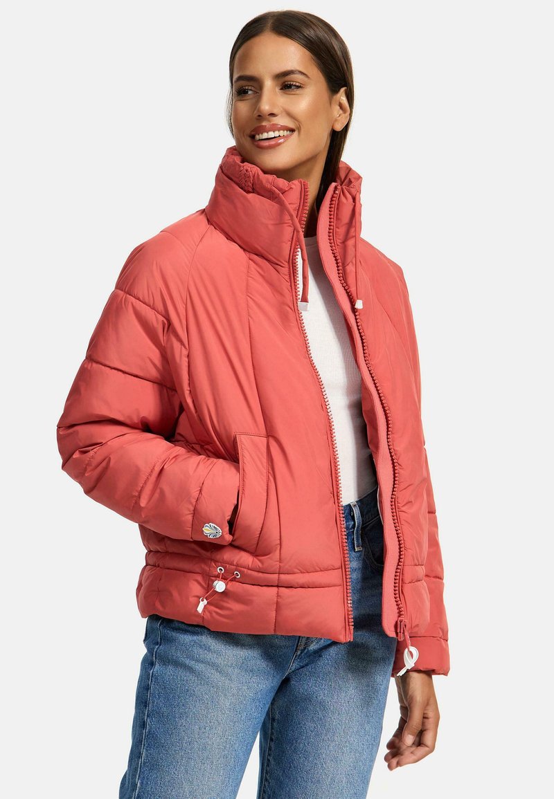 Dikke koraalkleurige jas met een hoge kraag, ritssluiting en twee voorzakken. Voorzien van trekkoorden in de taille en een decoratieve patch op de mouw.