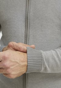 Grauer Reißverschluss-Pullover mit einem strukturierten Rippmuster, enganliegenden Bündchen und einem geraden Reißverschluss, der aus weichem Strickstoff gefertigt ist.