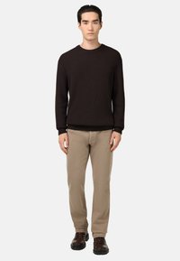 Suéter de punto acanalado oscuro, pantalones khaki claros y botas marrón con cordones. Diseño sencillo y ajustado con colores sólidos y un claro contraste de texturas.