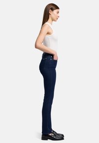 Ciemnoniebieskie dżinsy w slim fit, z wysokim stanem i pięcioma kieszeniami. W połączeniu z dopasowanym białym topem na ramiączkach i czarnymi mokasynami.