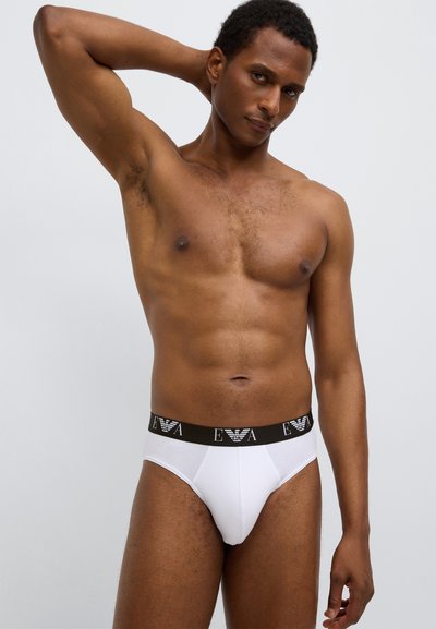 Mutande bianche con elastico nero in vita con il logo "EVA". Tessuto liscio con design aderente, che esalta forma e texture.