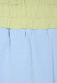 Két tónusból álló ruha sima textúrával; a felső rész világoszöld, gyűrött részletekkel, az alsó rész világoskék, pliszírozott.