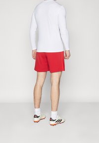 Pantalones cortos deportivos rojos y una camiseta de manga larga blanca, combinados con botas de fútbol de color claro con detalles en negro y naranja.