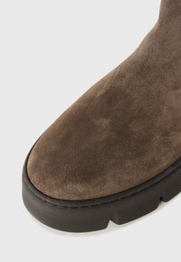 Bottine en daim marron avec un bout rond, surface texturée et semelle en caoutchouc noir épais. Présente un design sans couture et des coutures minimales.