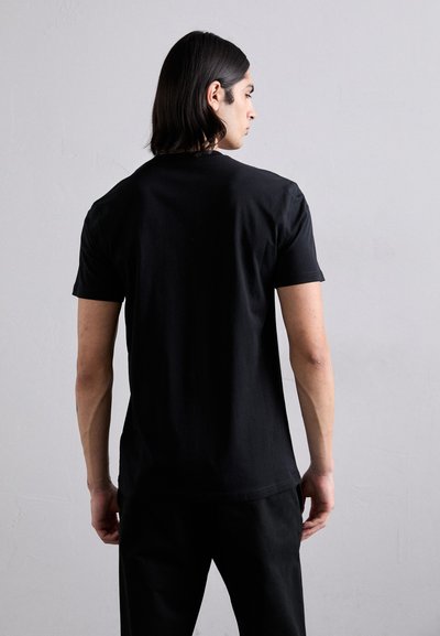 Black short-sleeve t-shirt, cotton material, round neckline, relaxed fit, smooth texture, worn with dark pants, viewed from the back.