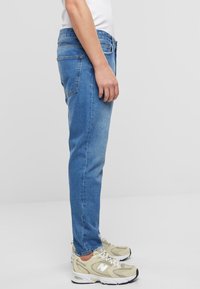 Vaqueros de mezclilla azul claro con un corte ajustado, que presentan bolsillos traseros y costuras en contraste, combinados con zapatillas beige.