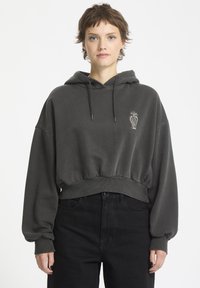 Ingekorte donkergrijze hoodie met een kangoeroezak, trekkoorden en een witte geborduurde wortelontwerp. Zachte textuur met ballonmouwen.