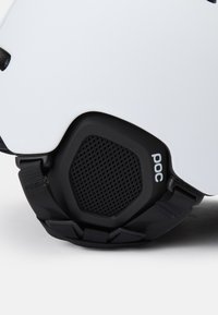 Weißer Helm mit schwarzen Akzenten, ausgestattet mit einem strukturierten schwarzen Netzbereich und verstellbaren Riemen für einen sicheren Sitz. Logo wird auffällig angezeigt.