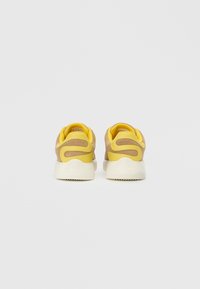 Zapatillas con parte superior beige, acentos amarillos y suela de goma blanca. Cuenta con paneles texturizados y un cuello acolchado para mayor comodidad.