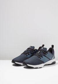 Pair of dark navy and black Nike training sneakers with white soles displayed on a white surface against a light background.