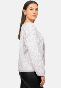 Maglione lilla con un motivo a stampa animale bianca, texture lavorata a maglia, spalle calate e fitting ampio, abbinato a leggings neri.