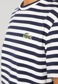 Marinblå och vit randig kortärmad skjorta med en liten grön krokodil-logotyp broderad på bröstet.