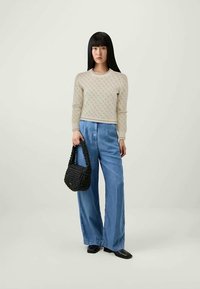 Beige Strickpullover mit strukturiertem Muster, hellblaue weitgeschnittene Jeans und eine kleine schwarze geflochtene Handtasche. Das Outfit zeichnet sich durch eine neutrale Farbpalette aus.