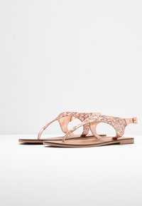 Roze gouden glitter sandalen met een open teen ontwerp, platte zool en verstelbare enkelband. Gemaakt van soepel materiaal en in een minimalistische stijl.