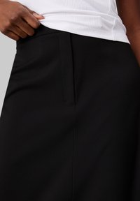 Jupe noire ajustée avec une texture lisse, des plis latéraux subtils et une taille cintrée, associée à un haut blanc à côtes.