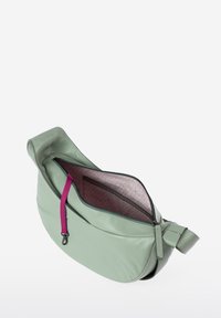 Borsa in pelle verde dalla forma arrotondata. La zip aperta rivela una fodera a motivo rosa e una tasca interna chiusa con un pull tab coordinato.