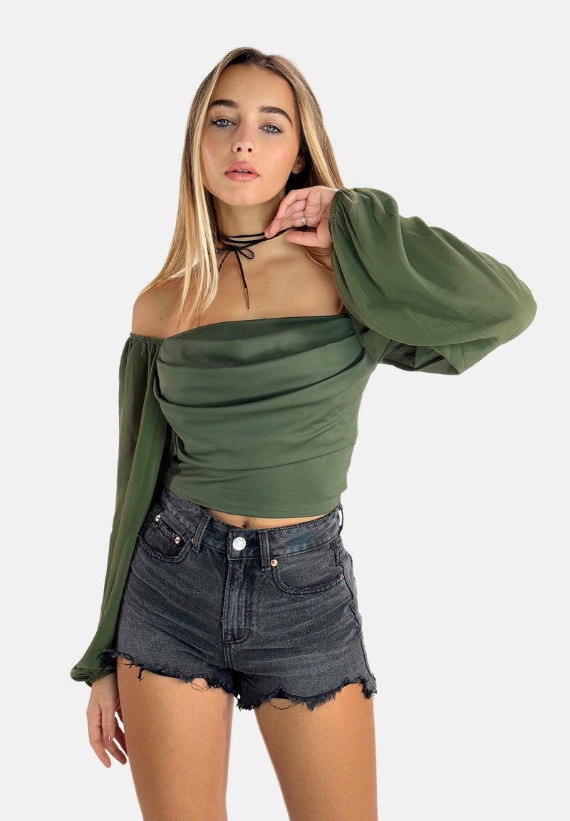 Top verde oliva scollato con maniche ampie, abbinato a pantaloni shorts in denim nero sfilacciati. Il top presenta una vestibilità aderente e una texture liscia.