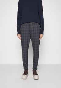 Grå rutiga byxor med dragsko i midjan, i kombination med en marinblå långärmad topp och beige och bruna snörkängor.