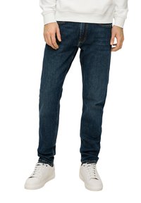 Jeans en denim bleu foncé avec une coupe ajustée, un design à cinq poches et des coutures contrastantes, associés à des baskets blanches pour un look décontracté.