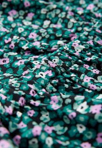 Tessuto stampato con piccoli fiori verdi, viola e bianchi su uno sfondo nero, con una superficie leggermente testurizzata e una caduta morbida.