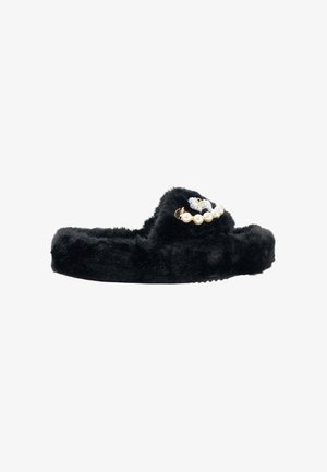 Zapatilla de pelaje negro con forma redondeada, que presenta un acento floral de perla y metal en la parte superior. Textura suave y diseño de suela plana.