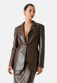 Blazer in pelle marrone con scollo profondo a V, rever a lancia e maniche lunghe. Tessuto liscio e vestibilità su misura. Presenta tasche laterali.