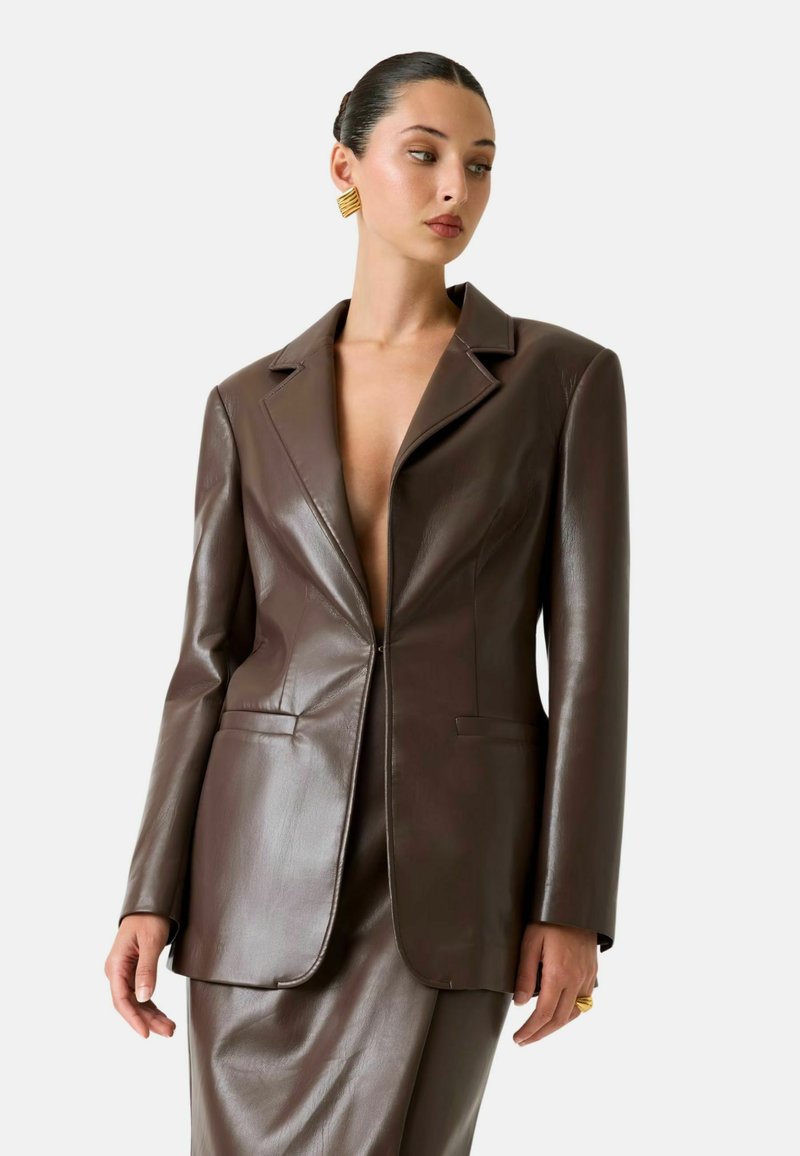 Blazer in pelle marrone con scollo profondo a V, rever a lancia e maniche lunghe. Tessuto liscio e vestibilità su misura. Presenta tasche laterali.