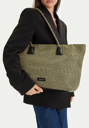 Žena v černém saku držící velkou pletenou černo-béžovou tašku na rameno s koženými uchy a štítkem "Lasocki".