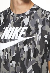 Grå kamouflage t-shirt i bomull med en framträdande vit Nike-logotyp över bröstet. Kortärmad och med rund hals.