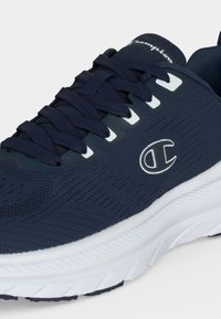 Chaussure de running Champion bleu marine avec semelles blanches, dessus en mesh, fermeture à lacets et logo Champion sur le côté et la languette.