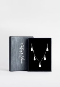 Silverhalsbandet visas i en svart låda och har fem tårformade hängsmycken fästa vid ett fint kedjor. Lådan har en texturerad blå utsida.