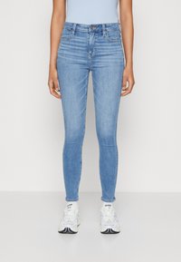 Lys blå skinny jeans i denim, med midjehøyde, fem lommer og en glatt tekstur. Nederkantene er frynset ved anklene.