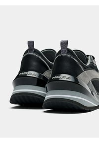 Chaussures de sport noires et grises avec une tige en maille, des accents en daim, des détails réfléchissants et une semelle épaisse et rembourrée avec un logo sur le talon.