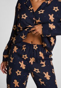 Navy pyjamaset met patronen van peperkoekkoekjes en sterren. Zachte stof, langmls knoopshirt en broek met elastische taille.