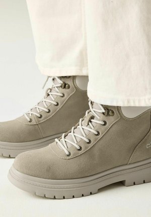 Bottines beiges en daim à lacets avec semelles robustes, portées avec un pantalon écru.