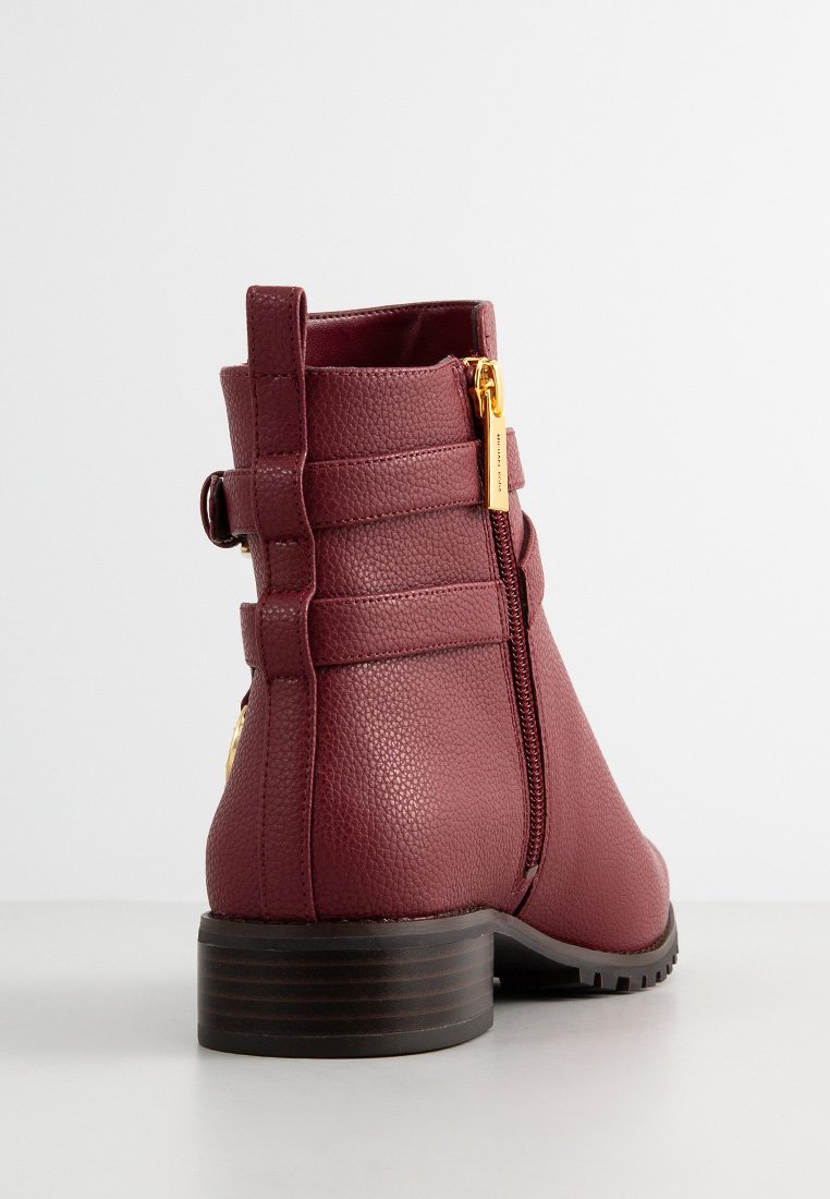 Burgunderfarbene Knöchelstiefel mit strukturiertem Lederfinish, seitlichem Reißverschluss, dekorativen Riemen und einem robusten braunen Absatz.