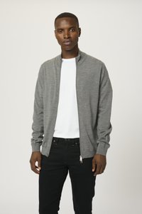 Grå zip-up kofta med en lätt textur, ribbade ärmmuddar och hög krage, lagd över en vit t-shirt och ihop med svarta byxor.