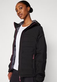 Black puffy jacket with grey accents, featuring a hood, zippered pockets, and pink zipper details. Lightweight and insulated design.