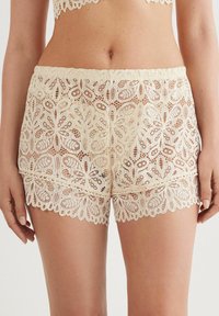 Ivoor kleurige kant shorts met een ingewikkeld bloemmotief, golfvormige randjes en een elastische tailleband voor een comfortabele pasvorm.