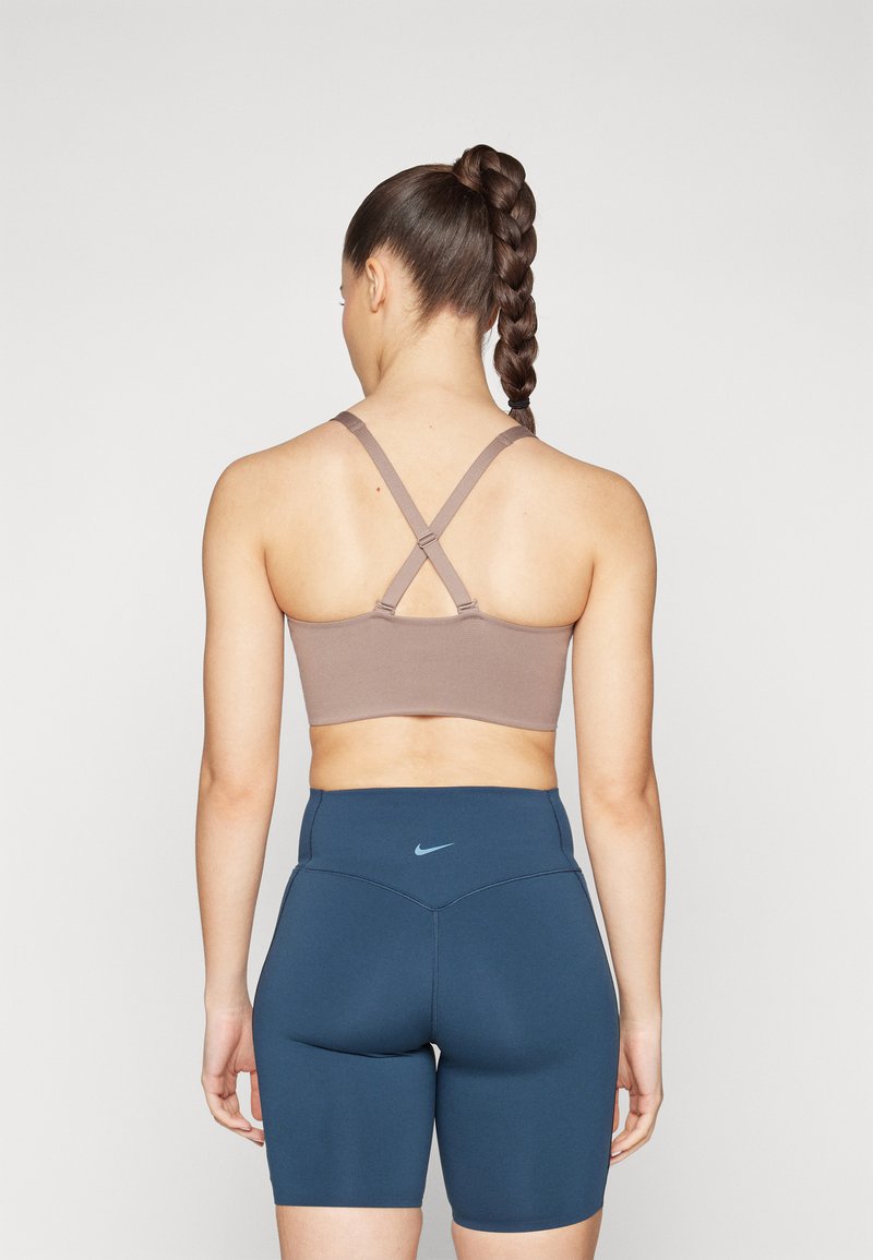 Brauner sportlicher Crop-Top mit überkreuzten Trägern, kombiniert mit blauen High-Waist-Shorts. Sanfte Textur mit minimalem Branding auf beiden Teilen.