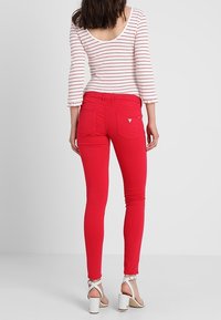 Jean skinny rouge avec poches arrière, associé à un haut à manches longues rayé et des talons blancs à lanières. Texture lisse, coupe près du corps.