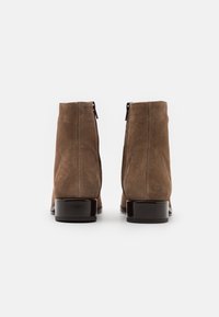 Bottines en suède marron avec une finition lisse, dotées de talons blocs noirs et de fermetures éclair à l'arrière pour un enfilage facile. Design simple et élégant.