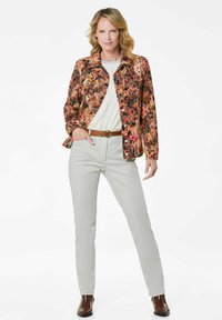 Bloemenpatroon jas in levendig oranje, roze en zwart met een knoopsluiting aan de voorkant, gecombineerd met lichtgrijze slim-fit broek en bruine laarzen.