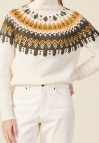 Pletený svetr v krémové barvě s vzorovaným sedlem, zdobený oranžovými, zelenými a tmavě žlutými akcenty. Vysoký límec a žebrované manžety.