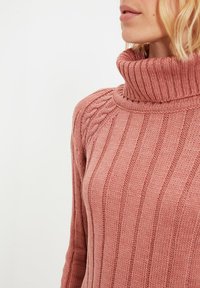 Rosafarbener Strickpullover mit hohem geripptem Kragen, ausgestattet mit vertikalen Streifen und Zopfmuster-Akzenten auf der Schulter.