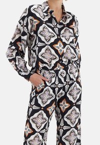 Camisa de botones en blanco y negro con estampado, de manga larga, que presenta motivos decorativos en naranja y lavanda, combinada con pantalones a juego.