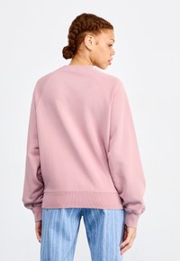 Sweatshirt rose avec un col rond et des poignets côtelés, présentant une texture lisse. Associé à un pantalon rayé bleu.
