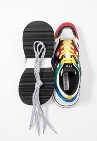 Zapatilla multicolor hecha de materiales sintéticos y de tela. Presenta acentos en rojo, azul, verde y negro, suela texturizada y cordones planos con patrón.