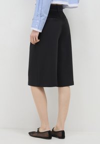 Culotte nere in morbido tessuto, caratterizzate da un design sartoriale con finitura liscia e dettagli di cucitura discreti. Abbinati a ballerine nere.