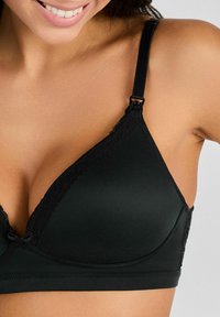 Sostén triangular negro hecho de material suave, con encaje en los bordes y tirantes ajustables con un cierre de plástico.